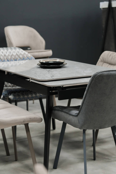 Серый деревянный стол в сочетании с бежевыми деревянными стульями с мягкой обивкой ткани. Голубые фарфоровые тарелки на столе - Фото, изображение