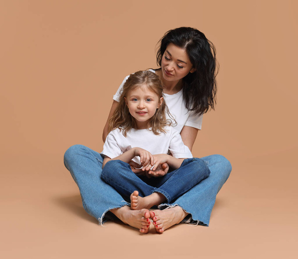 Beautiful mother with little daughter sitting on beige background - Valokuva, kuva