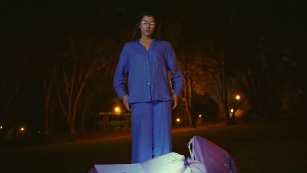 Kobieta wyglądająca na sprzątaczkę środowiska stoi nad świecącymi workami na śmieci. Piękny model pozujący w niebieskim garniturze otoczony nocnym spokojem w parku. Wykonawca mody wykazujący ekologiczny aktywizm. - Materiał filmowy, wideo