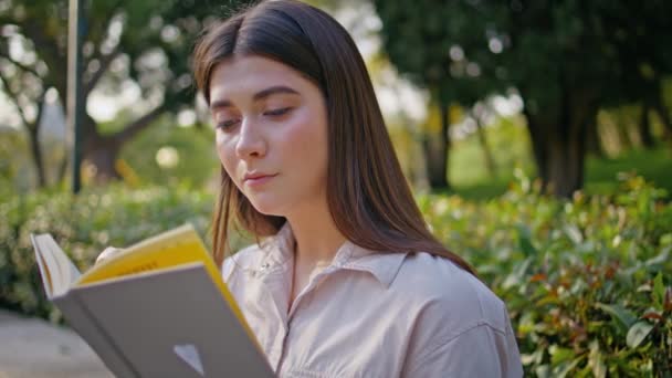 Portret student gericht op het lezen van boek op zonnige groene tuin. Close-up serene vrouwelijke lezer genieten van rustige natuur voor studie. Jonge mooie vrouw met roman in zittend levendig park bij zonlicht. - Video