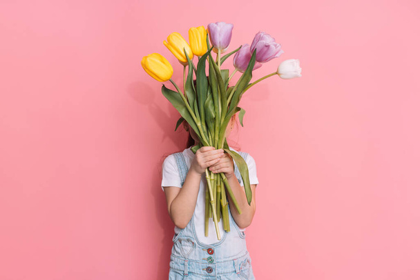 Ребенок держит букет тюльпанов на розовом фоне. - Фото, изображение
