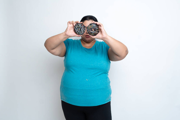 Overweight fat indian woman holding donuts in front of eyes and enjoying. isolated over white background. Plus size female. unhealthy eating. Copy Space - Fotografie, Obrázek