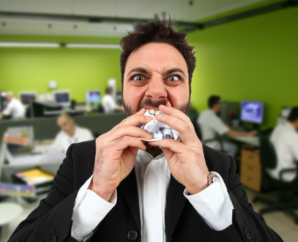 Wütender Geschäftsmann isst im Büro Papierschnipsel. - Foto, Bild