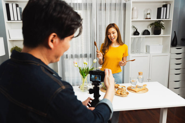 Asian beautiful woman food specialist blogger teaching how to mixed salad easy cooking in glass blow on live channel recorded by smart cameraman streaming lifestyle on social media concept. Infobahn. - Photo, Image