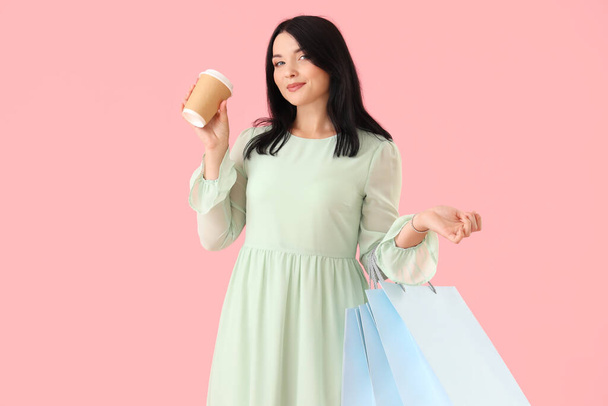 Beautiful young woman with shopping bags and cup of coffee on pink background - Photo, Image