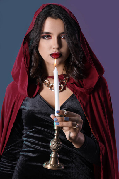Jeune sorcière avec bougie allumée sur fond de couleur sombre - Photo, image