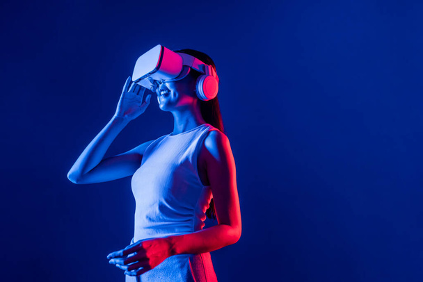 Έξυπνο γυναικείο stand με surrounded by cyberpunk neon light wear VR headset connecting metaverse, φουτουριστικό τεχνολογία κοινότητας κυβερνοχώρου. Κομψό γυναίκα ματιά δημιουργείται εικονική περιοχή. Ψευδαίσθηση. - Φωτογραφία, εικόνα