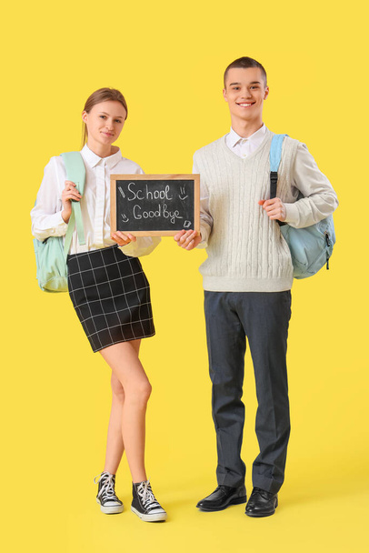 Studenti in possesso di lavagna con testo SCUOLA GOODBYE su sfondo giallo. Concetto di fine scuola - Foto, immagini