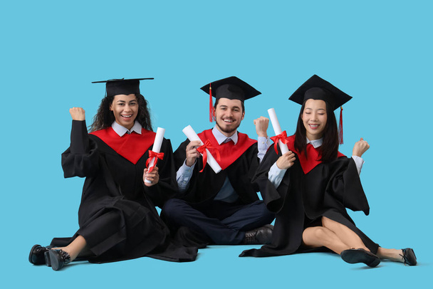 Absolwenci z dyplomami siedzącymi na niebieskim tle - Zdjęcie, obraz