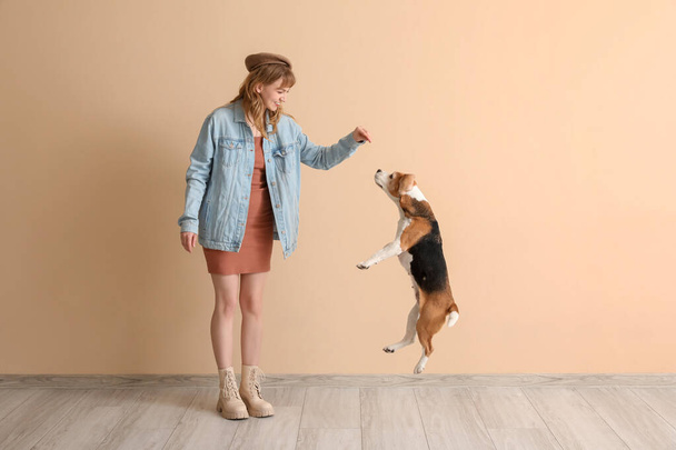 Giovane donna in abbigliamento casual giocare con simpatico cane beagle su sfondo beige - Foto, immagini