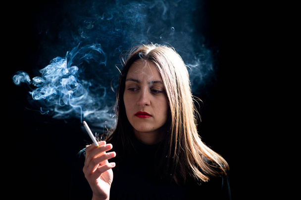Молода жінка палить сигарету на чорному тлі
 - Фото, зображення