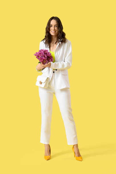 Stijlvolle jonge vrouw met tulpen op gele achtergrond - Foto, afbeelding