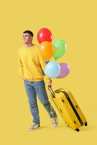 Młody człowiek z walizką i bandą balonów na żółtym tle - Zdjęcie, obraz