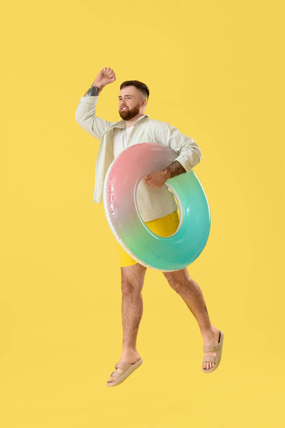 Giovane uomo con anello gonfiabile che salta su sfondo giallo - Foto, immagini