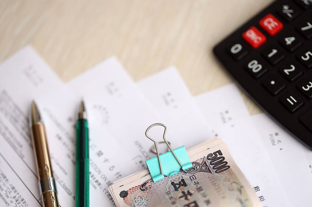 Japanse belastingformulieren ligt op tafel met rekenmachine, pen en Japanse yen geld rekeningen rollen close-up - Foto, afbeelding