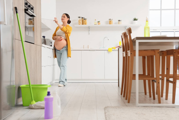 Mujer embarazada joven limpieza armario en la cocina - Foto, Imagen