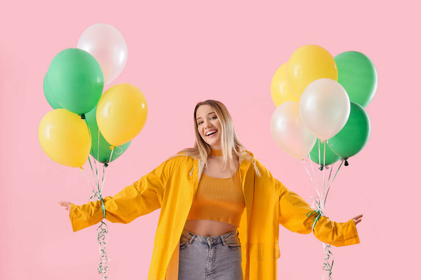 Young woman in raincoat with balloons on pink background - Photo, Image