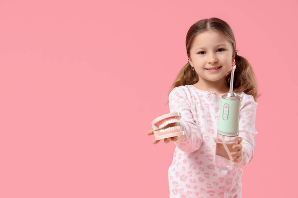 Carino bambina con irrigatore orale e modello di mascella su sfondo rosa - Foto, immagini
