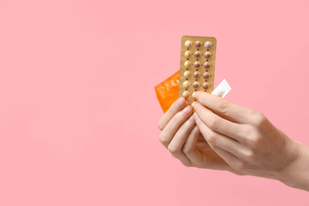 Kobiece dłonie z tabletkami antykoncepcyjnymi, czopkami i prezerwatywą na różowym tle - Zdjęcie, obraz