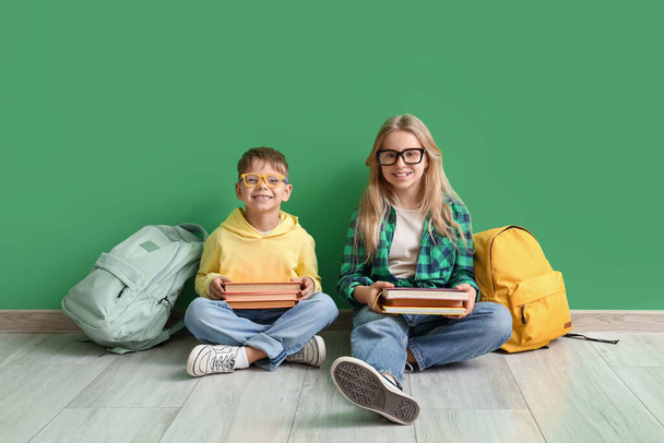 Симпатичні маленькі учні в окулярах з книгами, що сидять біля зеленої стіни - Фото, зображення
