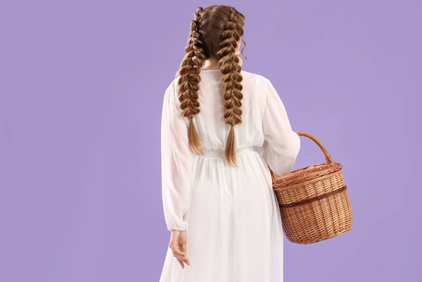 Hermosa joven con trenzas sosteniendo cesta sobre fondo lila - Foto, Imagen