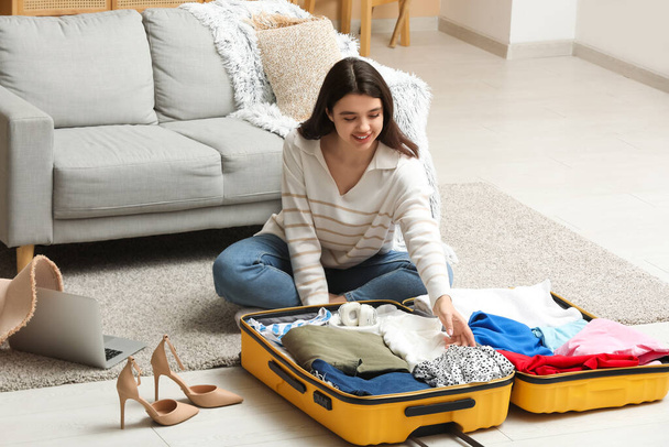 Junge Frau packt Koffer mit Kleidung im Wohnzimmer - Foto, Bild