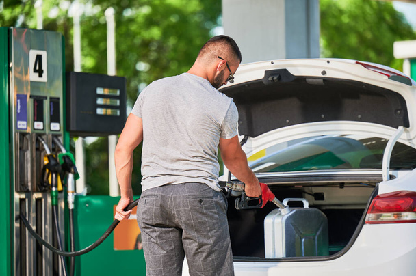Young man refueling canister with fuel. Skilled driver filling cistern with gasoline in case of unforeseen circumstances. Male adult with pump nozzle refueling canister in car trunk. - Photo, Image