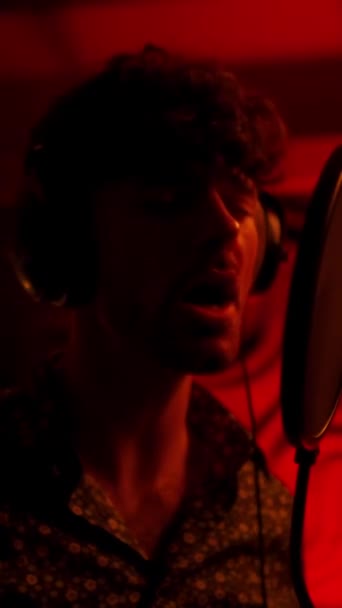 Singer man holding hands on headphones, while recording song in red light studio. Creative hobby concept - Footage, Video