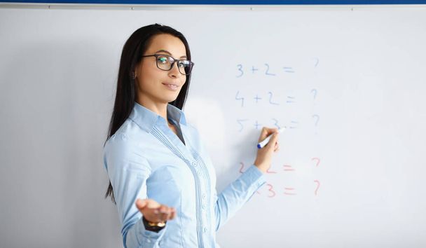 Profesora de pie en pizarra con fórmulas y explicando información. Clases de matemáticas para niños - Foto, Imagen