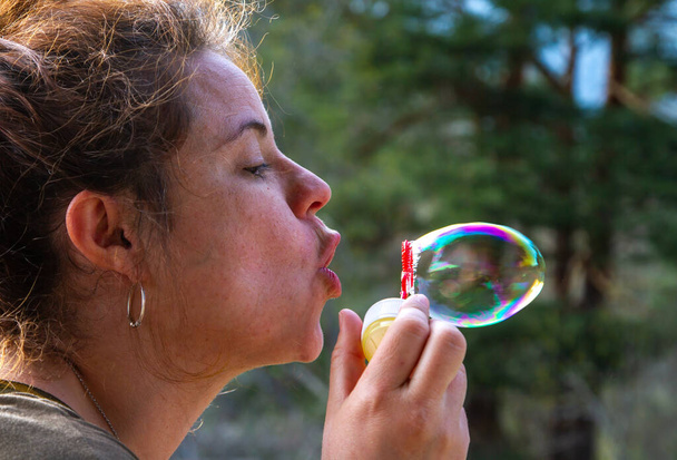 Гарненька молода жінка грає з мильними бульбашками в сонячний день - Фото, зображення