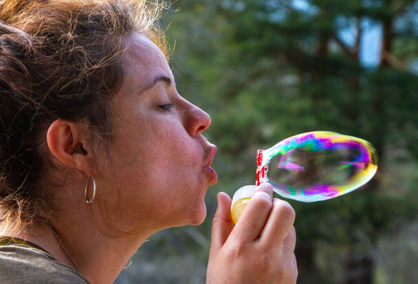 A pretty young woman plays with blowing soap bubbles on a sunny day - Photo, Image