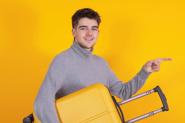 jeune homme isolé avec une valise de voyage pointant - Photo, image