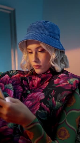 Mujer elegante de moda sentado en el sillón y navegar por Internet en el teléfono inteligente en el fondo del estudio por la noche - Imágenes, Vídeo