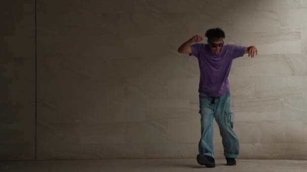 Zkušený chytrý pouliční tanečník cvičit b-boy pohyb v budově s šedým pozadím. Mladý pohledný choreograf provádí energický a aktivní pohyb. Venkovní sport2024. Vesele. - Záběry, video