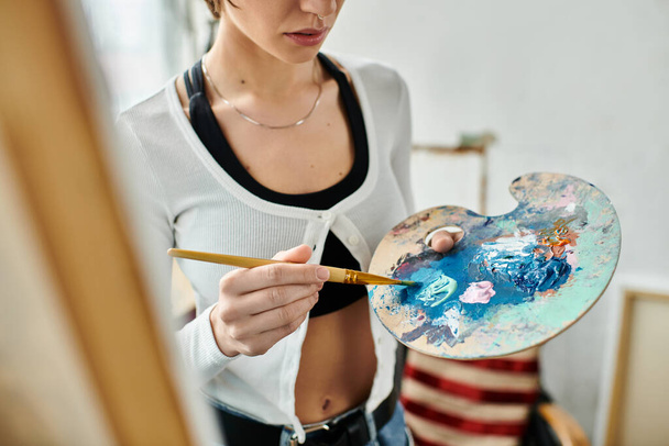 Egy nő finoman tart egy ecsetet és palettát, elmerülve a kreativitásban.. - Fotó, kép