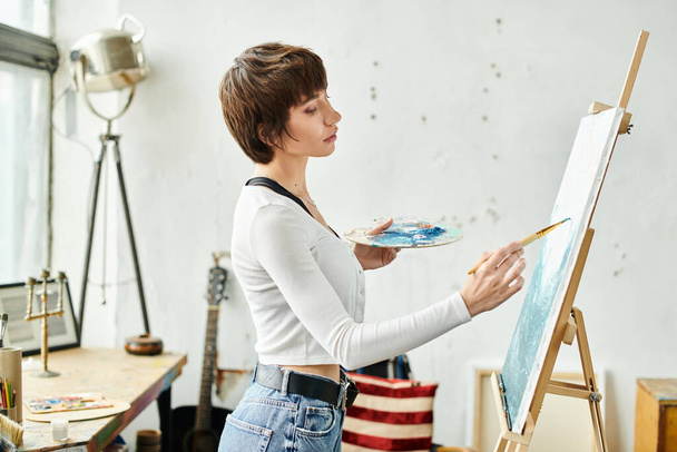 Женщина в белой рубашке рисует на мольберте. - Фото, изображение