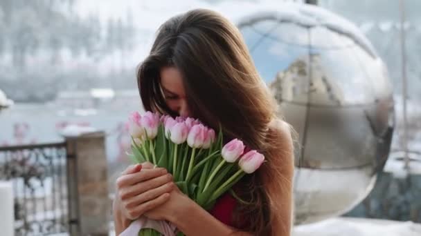 Portré egy csinos nőről piros ruhában, friss tulipánokkal a hegyekben. A nő egy csokor virággal pózol a kamerába. - Felvétel, videó
