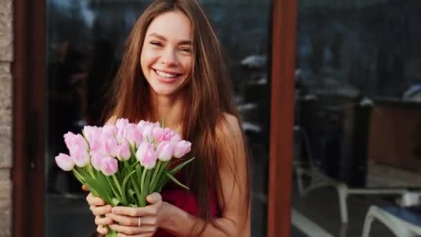 Portrait of a pretty woman in a red dress with fresh tulips in the mountains. The woman poses for the camera with a bouquet of flowers - Footage, Video