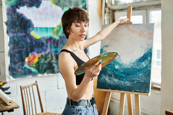 Μια γυναίκα ζωγραφίζει μια εικόνα με μια βούρτσα στο χέρι. - Φωτογραφία, εικόνα