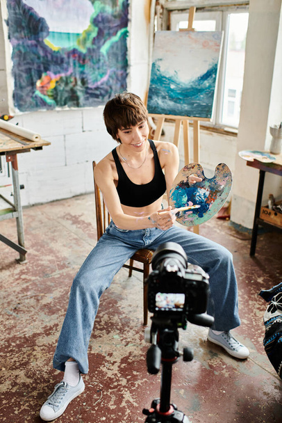 Μια γυναίκα κάθεται σε μια καρέκλα, κρατώντας έναν πίνακα με στοχαστική έκφραση. - Φωτογραφία, εικόνα