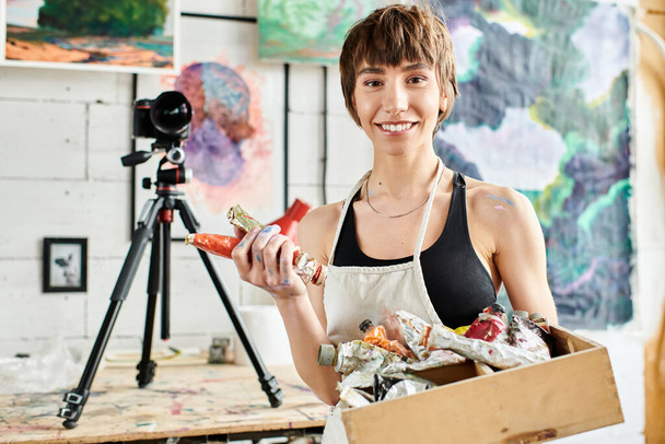 Una mujer sosteniendo una caja de pintura delante de una cámara. - Foto, imagen