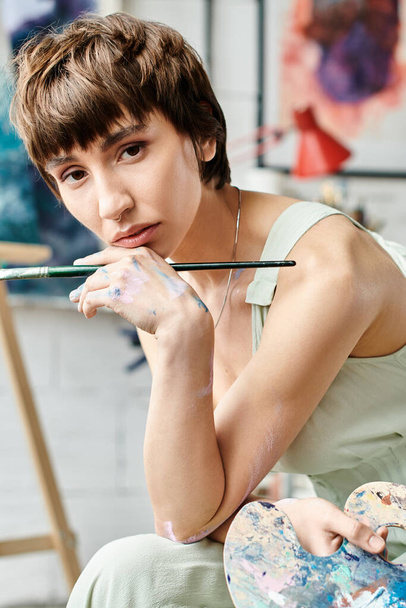 Vonzó nő ül egy festőállvány előtt egy ecsettel. - Fotó, kép