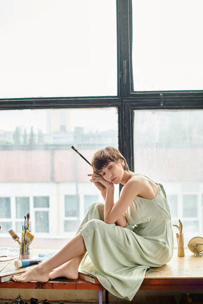 Una donna si siede con grazia accanto a una finestra, bagnata da una morbida luce naturale.. - Foto, immagini