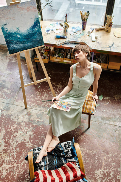 Uma mulher senta-se diante de uma pintura em uma cadeira. - Foto, Imagem