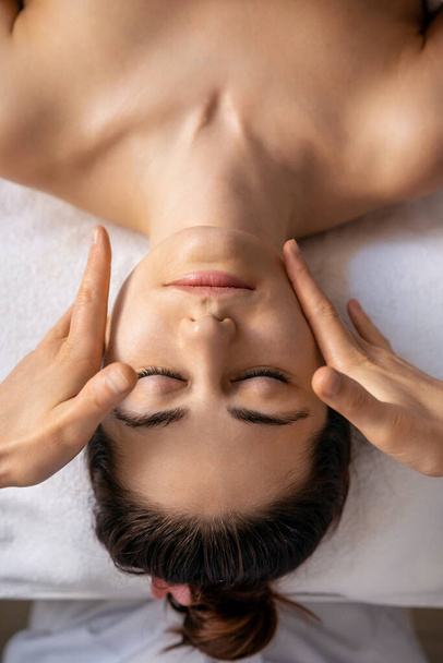 Top uitzicht op jonge vrouw krijgen spa massage behandeling bij beauty spa salon. Gezichtsschoonheid behandeling. Gezichtsmassage. Spa huid- en lichaamsverzorging. - Foto, afbeelding