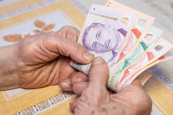 Mãos de uma mulher idosa segurar vários dólares de Singapura em suas mãos, Conceito econômico, Orçamentos domésticos de aposentados em Singapura, aumento do custo de vida e despesas - Foto, Imagem