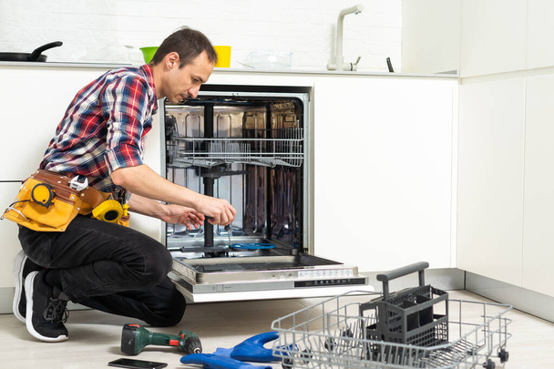 Uitzicht op de mens in het algemeen reparatie afwasmachine in de keuken. Hoge kwaliteit foto - Foto, afbeelding