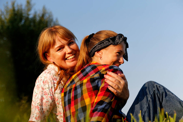 Un retrato conmovedor de una madre y su hija compartiendo un tierno abrazo al aire libre en un día soleado de verano, irradiando felicidad y amor familiar, perfecto para ilustrar momentos de unión familiar. - Foto, imagen