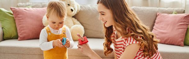 Eine junge Frau und ihre kleine Tochter spielen fröhlich mit einem Spielzeug und schaffen zu Hause gemeinsam besondere Erinnerungen. - Foto, Bild