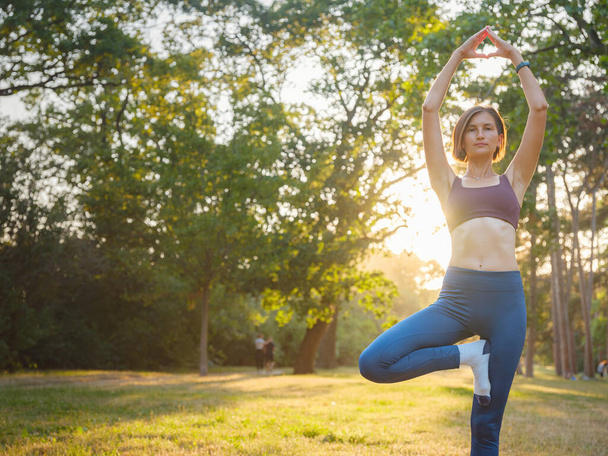 Молода азіатка робить йогу вранці або ввечері в парку, здорова жінка розслабляється і практикує позу на дереві в міському парку. Уважність, знедоленість, здорові звички та концепція балансу - Фото, зображення